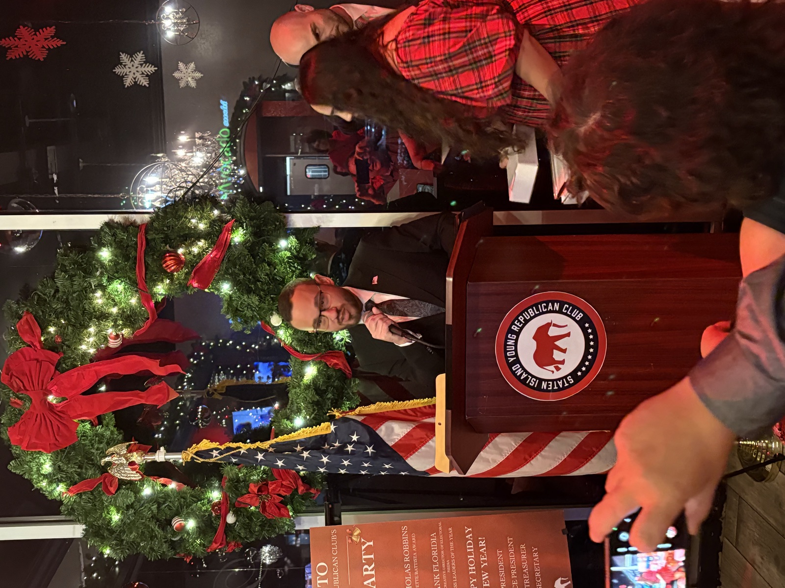 Nick Robbins speaking at a podium beside an American flag